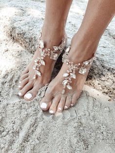 a woman's feet wearing barefoot sandals and jewelry on top of the sand at the beach