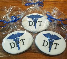 three decorated cookies sitting on top of a wooden table next to plastic wrappers and blue ribbon