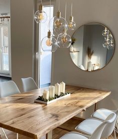 a dining room table with white chairs and candles on the centerpiece, in front of a round mirror