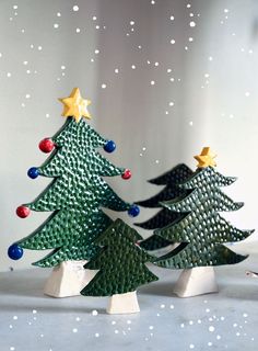 three small christmas trees with stars on them in front of a snow covered wall and white background