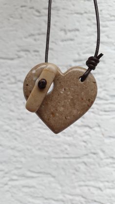 a heart shaped stone hanging from a leather cord on a white brick wall with a black bead