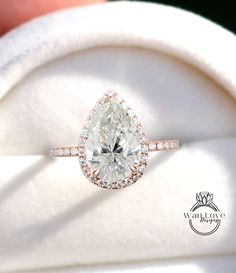 a close up of a person's hand holding an engagement ring with a pear shaped diamond