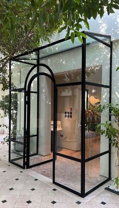 a black glass house sitting on top of a tiled floor next to a tree and potted plant