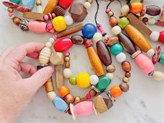 a hand is holding a bead necklace made out of wooden beads and other colorful beads