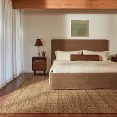 a large bed in a bedroom next to a window with curtains on the windowsill