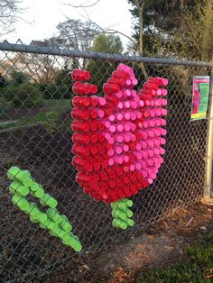 there are flowers made out of bottle caps on the fence and behind it is a chain link fence