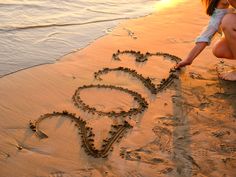 a woman kneeling down on the beach writing in the sand with her face drawn into the sand