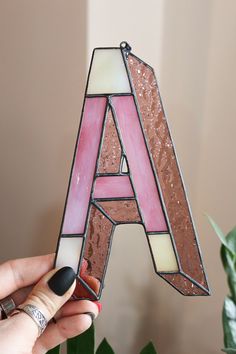 a woman holding up a stained glass letter with pink and white letters on it's sides