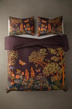 a bed with two pillows and purple comforter covers on top of it, in front of a gray wall