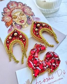 two red and gold brooches sitting on top of a white card next to a candle