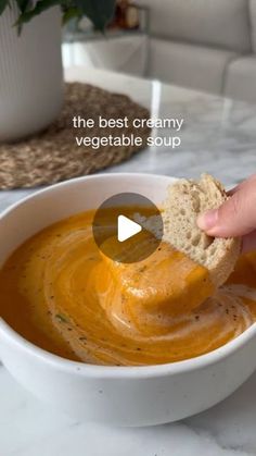 a person dipping something into a bowl of soup with a piece of bread in it