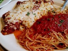 a white plate topped with pasta and meat covered in marinara sauce next to a fork