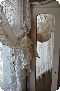 the curtains are hanging on the wall by the window in front of the mirror, which is covered with white lace