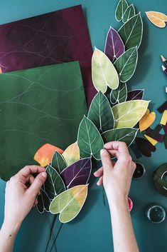 someone cutting out leaves on top of a piece of art paper with scissors and glue