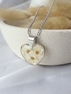 Heart shaped necklace, a harmonious blend of elegance and nature's beauty. Adorned with delicate dry spiraea flowers. The shimmering background adds a touch of radiance to the design, creating a captivating play of light that enhances the intricate detailing. Crafted from high-quality stainless steel, this piece exudes durability and longevity, ensuring it remains a cherished accessory for years to come. White Stainless Steel Necklaces For Mother's Day, Mother's Day White Stainless Steel Necklaces, Dainty Heart Pendant Jewelry With Birth Flower, Mother's Day Flower Shaped Jewelry With Heart Charm, Stainless Steel Heart Pendant Necklace For Mother's Day, Mother's Day Jewelry With Heart Charm And Flower Shape, Mother's Day Flower Jewelry With Heart Charm, Mother's Day Heart Pendant Necklace In Stainless Steel, Hypoallergenic Heart Shaped Stainless Steel Necklace