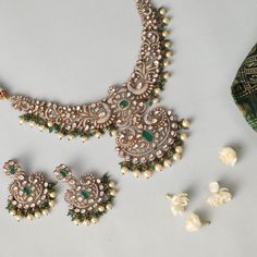 Description : Presenting our opulent floral and peacock motif necklace and earring set. This exquisite ensemble showcases meticulous craftsmanship, with moissanites and cubic zirconia stones arranged into intricate floral and peacock motifs, enhanced by Victorian plating for an added touch of old-world charm. The necklace drapes gracefully, adorned with green semi-precious gemstones and hanging pearls, while the matching earrings complete the look with similar motifs, offering a rich and regal e Elegant Jewelry Sets With Peacock Design And Chandbali Shape, Elegant Kundan Bridal Necklace With Peacock Design, Elegant Kundan Necklace With Peacock Design For Festive Occasions, Traditional Jewelry Sets With Diamond Accents, Elegant Festive Jewelry Sets With Peacock Design, Festive Diamond Bridal Sets With Intricate Design, Festive Elegant Kundan Necklace With Peacock Design, Elegant Chandbali Bridal Necklace With Peacock Design, Temple Jewelry Sets With Intricate Diamond Design