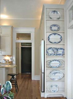 a narrow kitchen with white cabinets and blue plates on the shelves, along with hardwood flooring