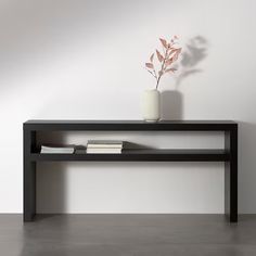 a vase with a plant on top of it next to a black shelf in a white room