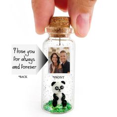 a hand holding a tiny glass bottle with a panda bear inside