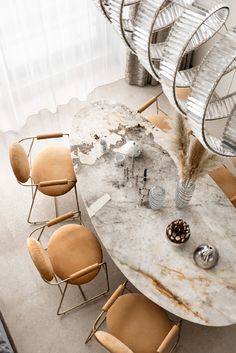 a marble dining table surrounded by chairs and vases with feathers on them, in front of a window