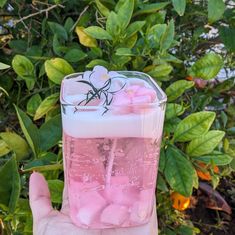 a hand holding a pink liquid filled with flowers