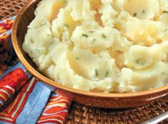 a brown bowl filled with mashed potatoes on top of a woven place mat next to a spoon