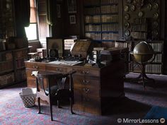 an old fashioned desk in the corner of a room with many bookshelves and other items