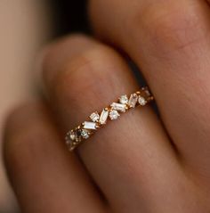 a woman's hand wearing a gold ring with white stones on the middle and sides