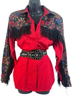 Add a touch of vintage style to your wardrobe with this black and red Adobe Rose western rodeo fringe cowgirl blouse. The blouse features a collared neckline, button closure, and long classic/fitted sleeves. The fringe accents and floral pattern add a unique touch to the blouse, making it perfect for any party or cocktail occasion. Made of 100% cotton, this blouse is machine washable and comes in a size M. The blouse is an authentic original vintage style, with a classic fit and size type. It is Long Sleeve Fringe Tops For Festivals, Fall Rodeo Long Sleeve Blouse, Red Western Long Sleeve Tops, Western Style Red Long Sleeve Tops, Fall Long Sleeve Blouse For Rodeo, Red Long Sleeve Western Top, Spring Long Sleeve Blouse For Rodeo, Western Style Blouse For Spring Rodeo, Vintage Tops For Western-themed Events