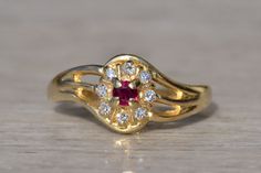 The Roseburg: Ladies 14K Ruby and Diamond Retro Ring. This stunning ring is crafted from 14 karat yellow gold and features a rich, lustrous shine that catches the eye. At the center of the ring sits a gorgeous, red ruby, which is cut in a classic round shape and held securely in place by delicate prongs. Surrounding the ruby is a glittering halo of diamonds, which adds an extra layer of sparkle and elegance to the design. The ring is currently a finger size 7.5 and is able to be resized for an a Heirloom Style Gold Ruby Ring With Brilliant Cut, Heirloom Gold Ruby Ring With Brilliant Cut, Luxury Gold Birthstone Ring With Halo Setting, Gold Ruby Ring With Center Stone, Gold Ruby Ring With Halo Setting For Anniversary, Elegant Gold Birthstone Ring With Halo Setting, Gold Ruby Wedding Ring 14k, Gold Ruby Ring With Brilliant Round Cut, Gold Rings With Brilliant Cut Ruby