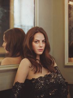 a woman sitting in front of a mirror wearing a black dress with sequins on it