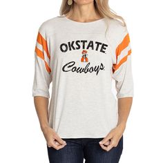 Elevate the style of your game day tee with this Oklahoma State Cowboys Sabrina Jersey T-shirt. It features the team name and logo accentuated by contrast-color side stitching and sleeve stripes. A rounded hem gives this Oklahoma State Cowboys shirt a more comfortable fit and feel. Collegiate Game Day T-shirt With Team Name, Varsity T-shirt For College Football Season, Varsity Jersey Tops For Fan Gear, Varsity Logo Print T-shirt For Game Day, Jersey Tops For Game Day, Sports Fan Style, Jersey Sports Fan Top For Game Day, Jersey Material Sports Fan Top For Game Day, Varsity Jersey T-shirt For Baseball Season, Casual Jersey T-shirt For Game Day