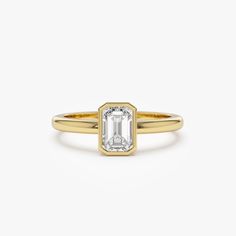 a yellow gold ring with an emerald cut diamond in the center, on a white background