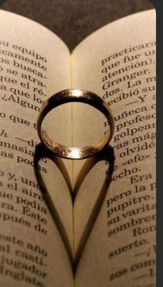 a ring casts a heart shaped shadow on an open book with the word love written in spanish