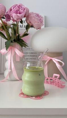 some pink flowers are in a vase on a white table and next to a lamp