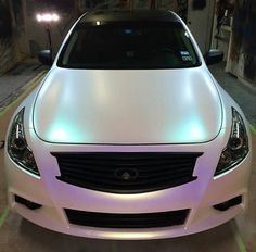 a white car parked in a parking lot with its lights on and the hood up