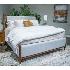 a bed sitting on top of a white rug next to a wooden dresser and lamp