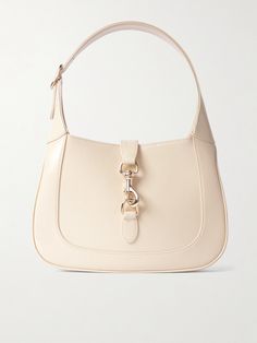 Gucci's small 'Jackie' bag takes its curved silhouette from the original style that debuted in the '60s and even boasts the same gold-tone piston clasp. Crafted in Italy from ivory patent-leather, it's suspended on a thick strap that can be adjusted to your perfect drop. It has plenty of space inside for everyday essentials, like your wallet, keys, cell and compact. White Luxury Designer Bag, Luxury High-end Women's Baguette Bag, Simple Designer Bags, Luxury Leather Miu Miu Shoulder Bag, Luxury Sleek Shoulder Baguette Bag, Affordable Luxury Bags, Hand Bag Outfit, Jackie Purse, Essentials Clothes