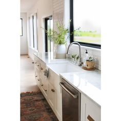 a kitchen with white cabinets and marble counter tops is pictured in this image, there are plants on the window sill