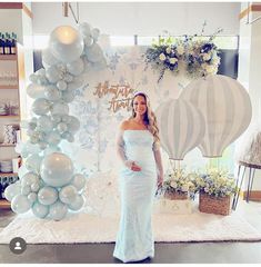 a pregnant woman standing in front of balloons at a baby shower with an air balloon arch