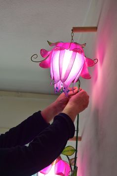 a person holding a pink light in their hand and hanging it from the ceiling above them