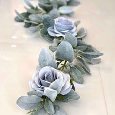 some blue flowers and green leaves on a white counter top in front of a mirror