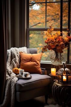 a chair and table in front of a window with candles on it, next to a vase filled with flowers