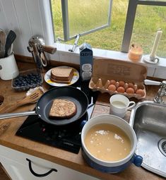 the kitchen counter is cluttered with food and utensils, such as eggs, toast, milk, butter, and water