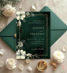 a green and gold wedding card on top of an envelope with white flowers in the background