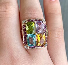 A multicolored gemstone ring, that is VERY. HEAVY on the gemstones, 14k Rose Gold, currently a size 5 1/4. The Gemstones are Blue Topaz, Citrine, Peridot, and Amethyst. There are 2 more citrine, and 2 blue topaz on the sides of the band. There is a darker purple amethyst halo around the large stones with 4 small diamond accents in the corners with white gold prongs on the small diamonds. 1x 6.0x7.5mm cushion cut light amethyst 1x 6.0x7.5mm cushion cut citrine 1x 6.0x7.5mm cushion cut blue topaz 1x 6.0x7.5mm cushion cut peridot 2x 5.0x2.9mm tapered rectangle citrine 2x 4.2x2.4mm tapered rectangle blue topaz 4x 1.2mm round diamonds 20x 1.6 round dark amethyst Fine Jewelry Multicolor Oval Gemstones, Multicolor Diamond Gemstones With Accents, Luxury Multicolor 14k Gold Gemstones, Luxury Multicolor Gemstones With Accents, Luxury Multicolor Multi-stone Gemstones, Luxury Multicolor Rings With Gemstone Accents, Fine Jewelry Multicolor Gemstones For Anniversary, Fine Jewelry Multicolor Gemstones With Accents, Multicolor Fine Jewelry Gemstones For Anniversary