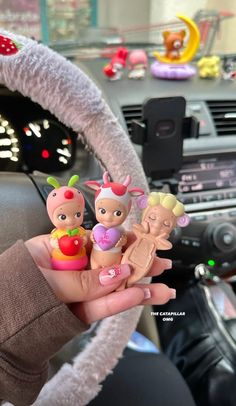 a hand holding a toy in the middle of a steering wheel with other toys behind it