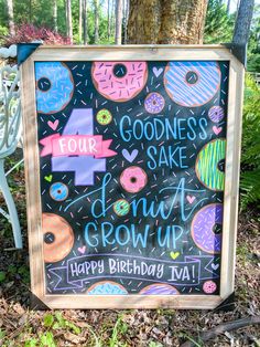 a chalkboard sign with donuts written on it in front of a bench and trees