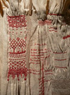 an old piece of cloth with red thread on it and clothes pins attached to the side