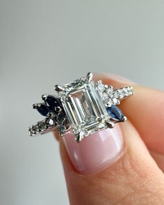 a woman's hand holding an emerald and blue sapphire ring with diamonds on it